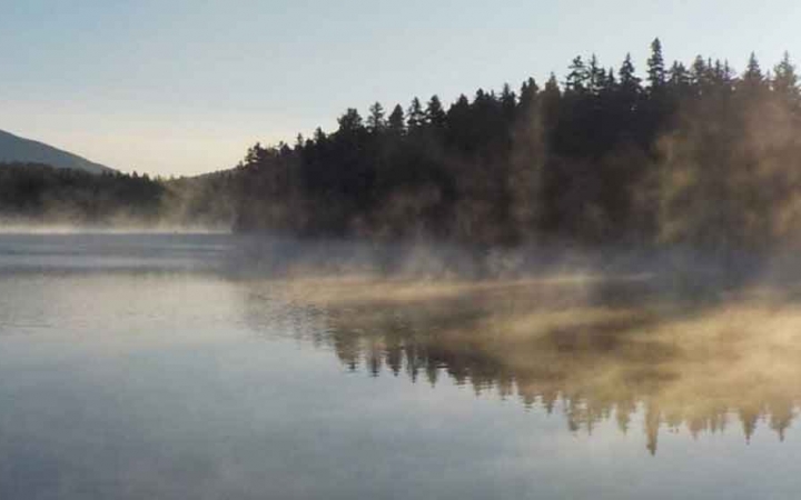 mist rises from still water at sunrise